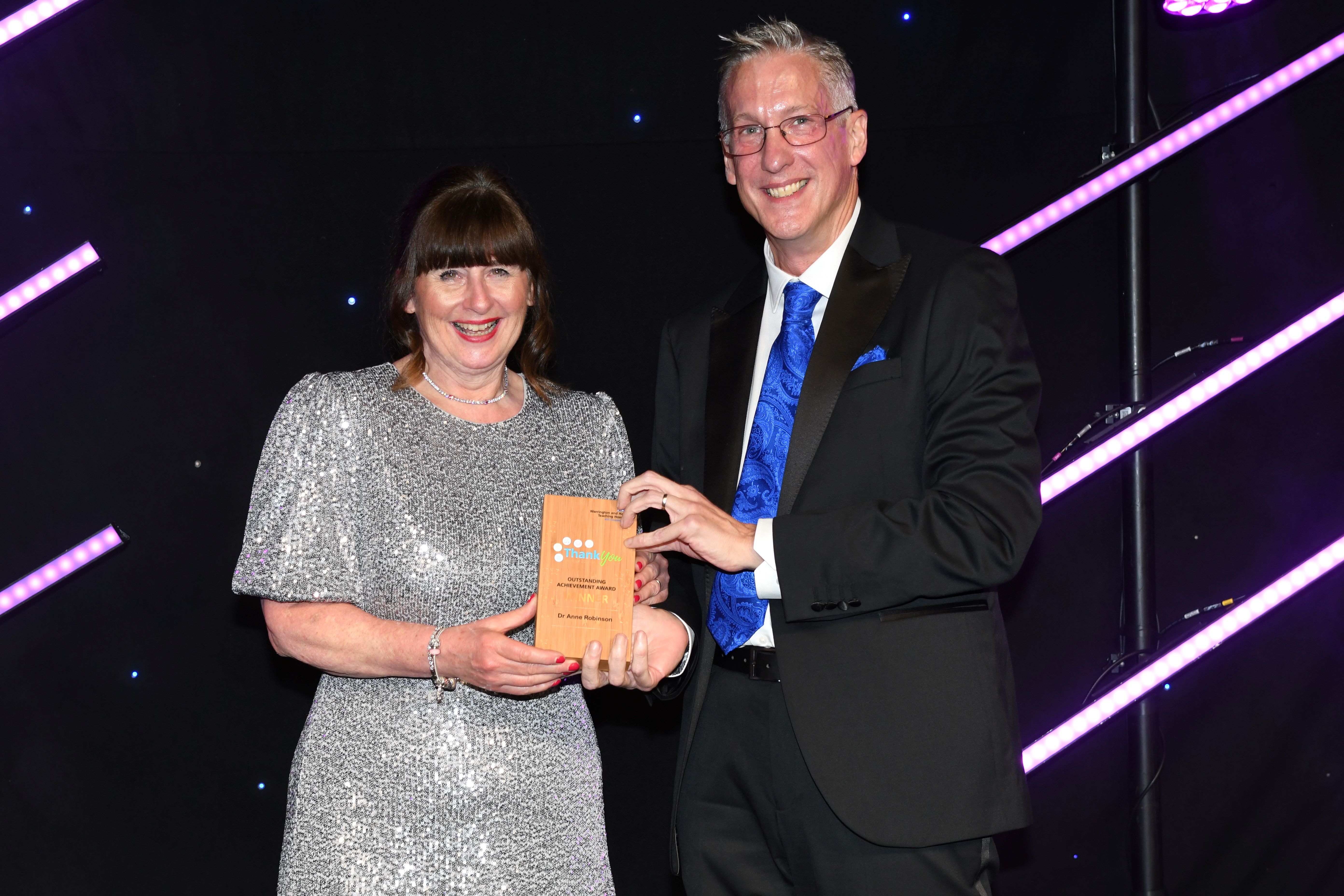 Dr Anne Robinson on stage, receiving her award from Simon Constable, CEO.